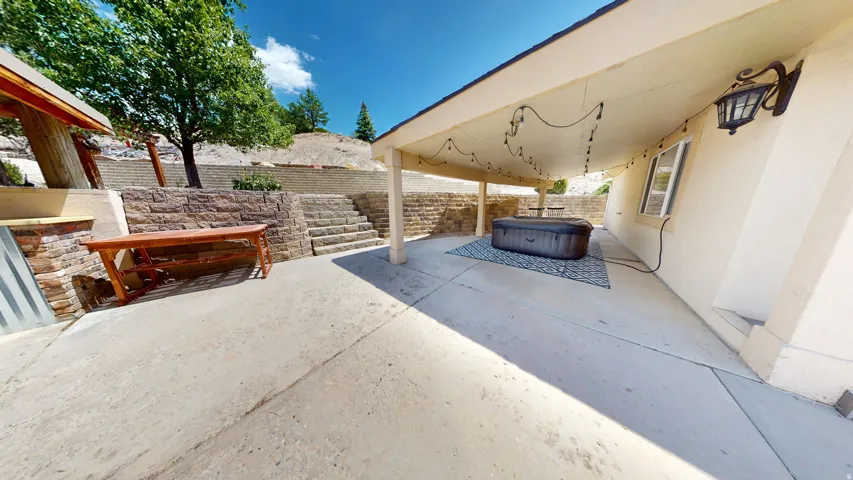 Expansive concrete patio featuring a covered area with string lighting and an exterior wall light fixture