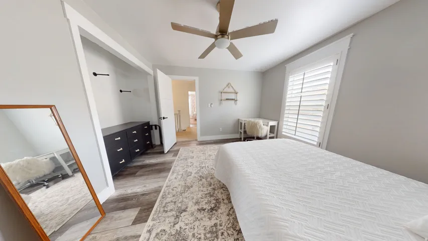 Spacious room featuring wood-finish flooring, a ceiling fan, and a window with plantation shutters