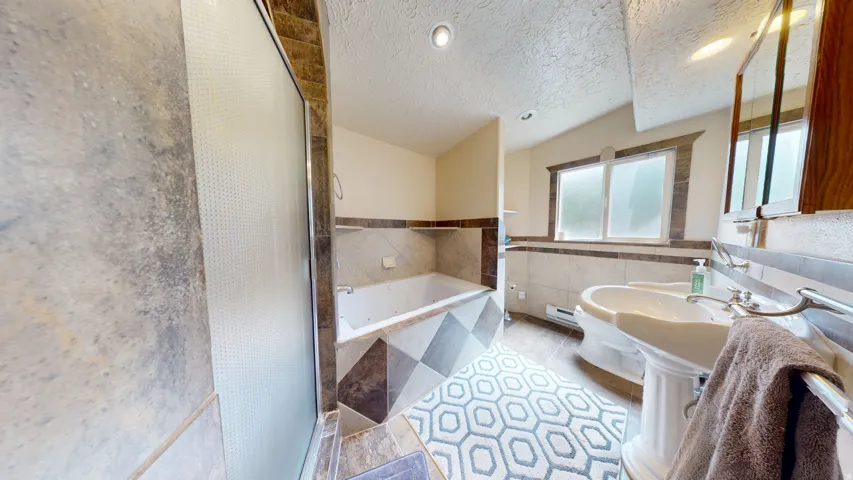 Bathroom featuring a pedestal sink, built-in tub, tiled walls with decorative accents, and a frosted window