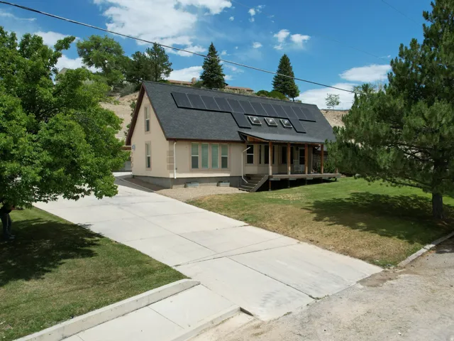 Beige exterior featuring a covered front porch, dark shingle roof with solar panels, and mature landscaping