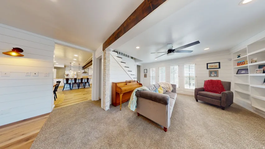 Carpeted living area featuring a ceiling fan, white shiplap walls, and multiple windows with plantation shutters