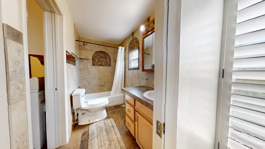 Bathroom with tiled walls, a built-in shower niche with mosaic tile, and a single vanity with wood-finish cabinetry