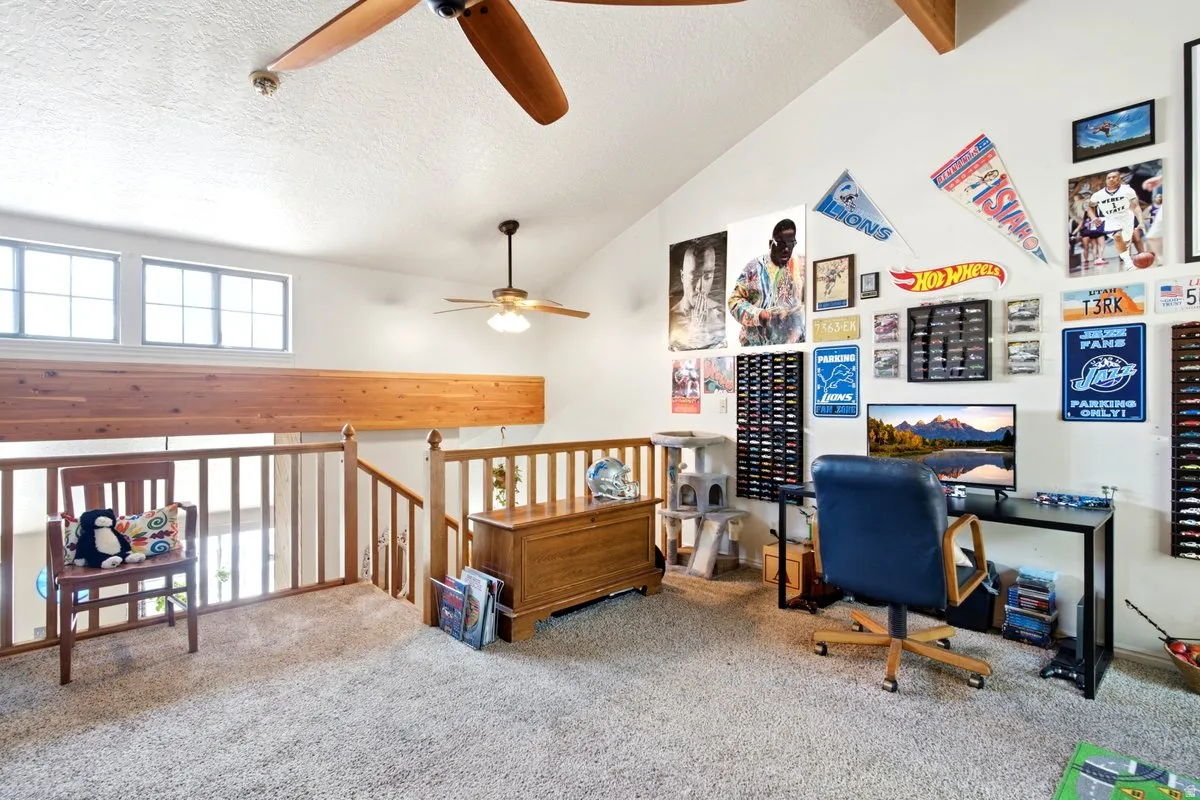 Carpeted loft area featuring a vaulted ceiling with exposed wood beams and two ceiling fans