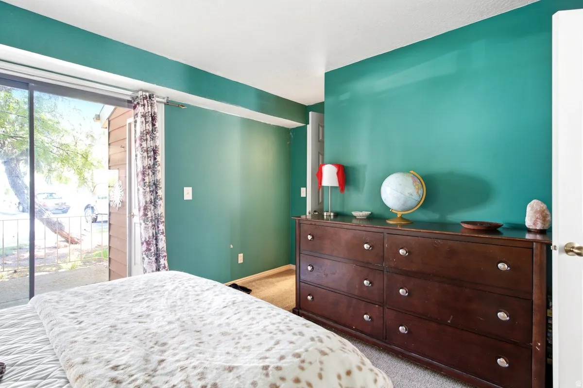Bedroom featuring a sliding glass door to a private patio, teal accent wall, and neutral carpeting