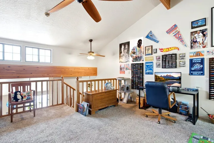 Carpeted loft area featuring a vaulted ceiling with exposed wood beams and two ceiling fans