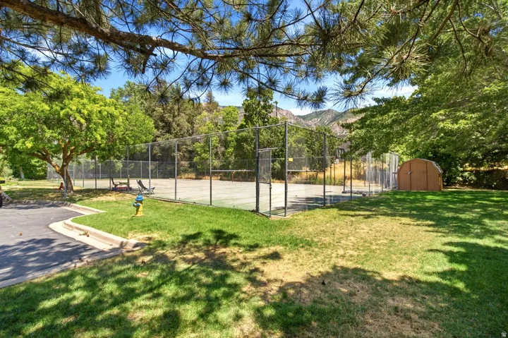 Fenced tennis court featuring a hard surface, surrounding green space, and a storage shed