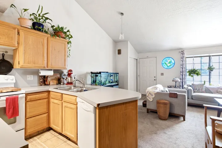 Vaulted ceiling kitchen featuring wood cabinetry, laminate countertops, a double basin stainless steel sink, and tile flooring