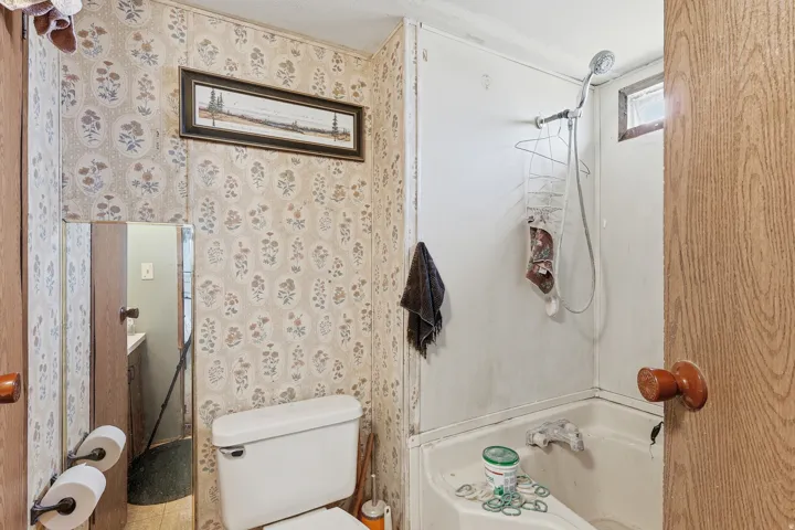 Bathroom featuring a shower and tub combination, white toilet, and patterned wallpaper
