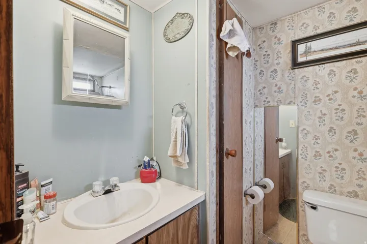 Bathroom featuring an integrated sink, laminate countertop, medicine cabinet, and patterned wallpaper