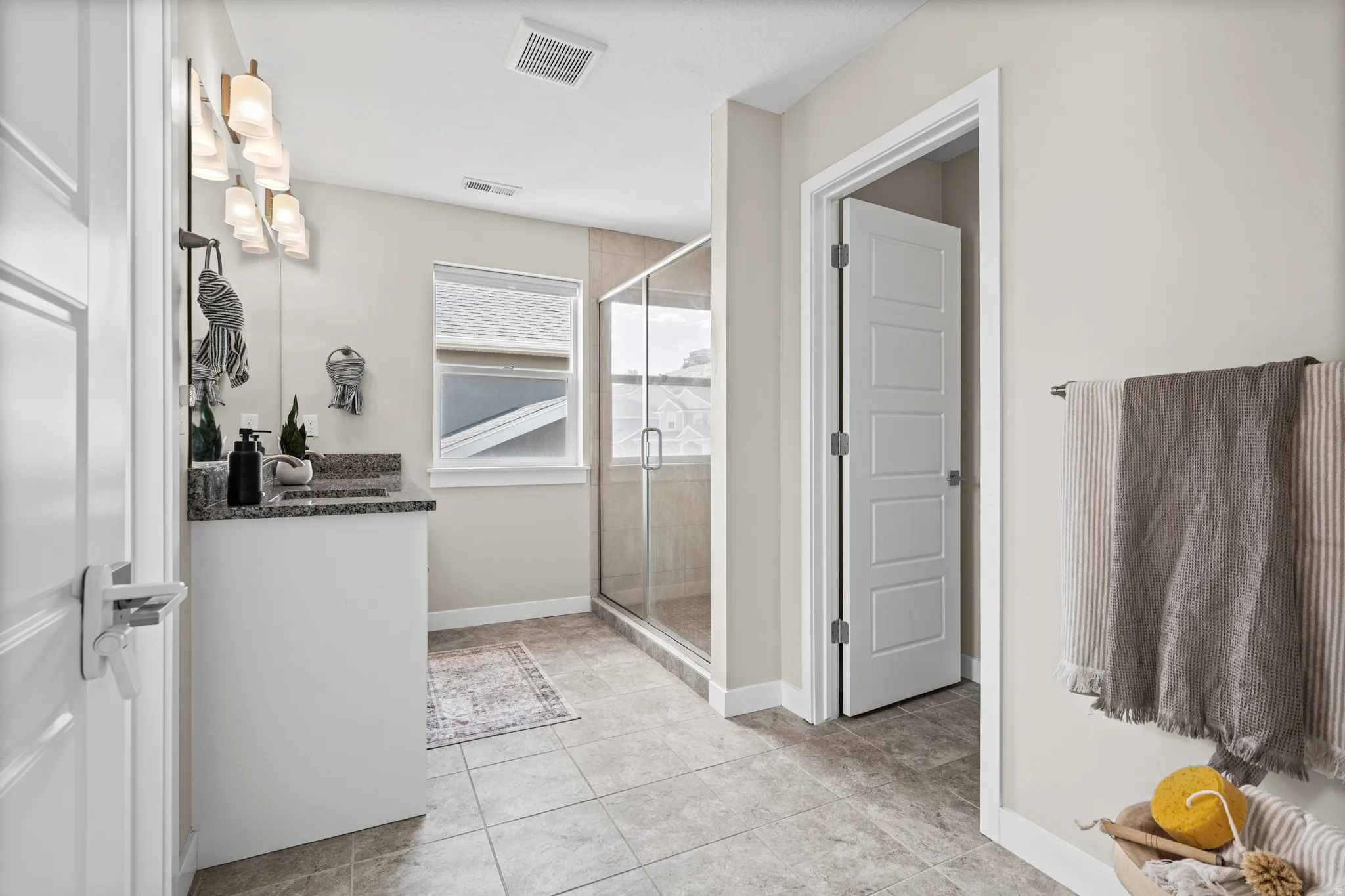 Bathroom featuring a single vanity with stone countertop, tile flooring, glass-enclosed shower, and a large window providing natural light