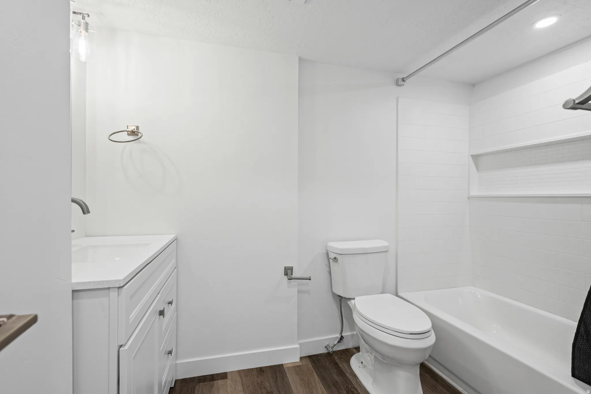 Bathroom featuring a white vanity with a solid surface countertop, a wall-mounted faucet, wood-finish flooring, a white toilet, and a bathtub with white subway tile surround
