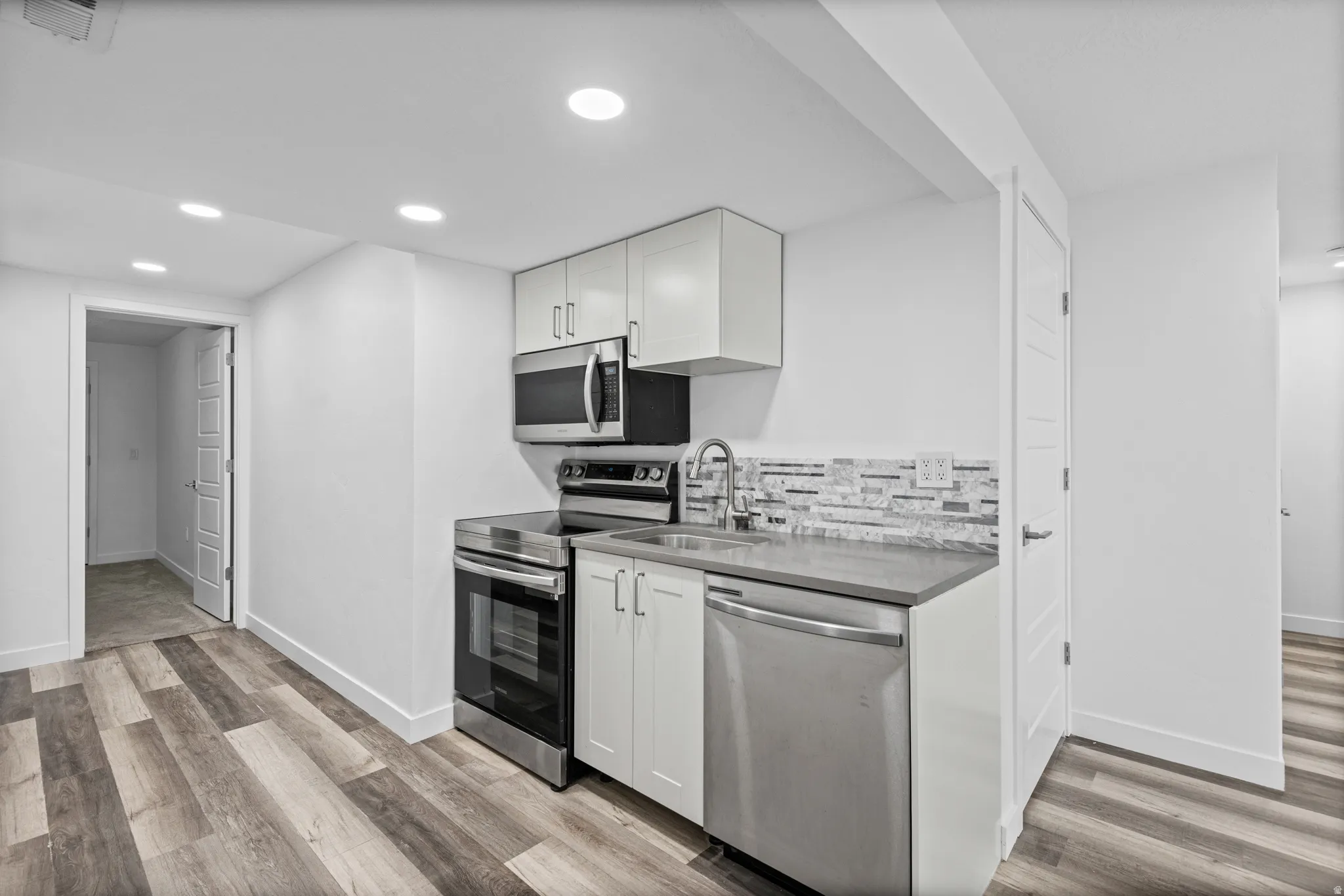 Compact kitchen area featuring stainless steel appliances, white cabinetry, and a textured tile backsplash