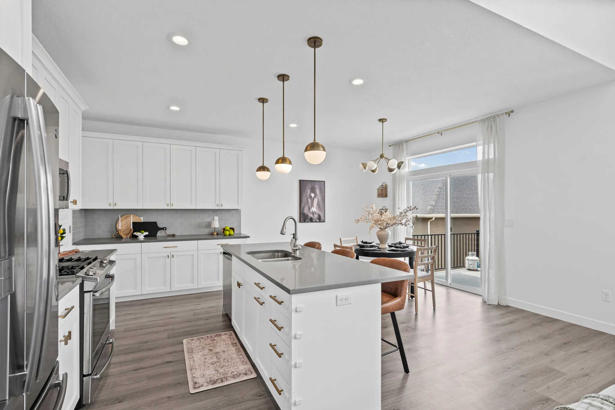 Modern kitchen featuring white cabinetry, stainless steel appliances, a center island with sink, quartz countertops, and wood-finish flooring