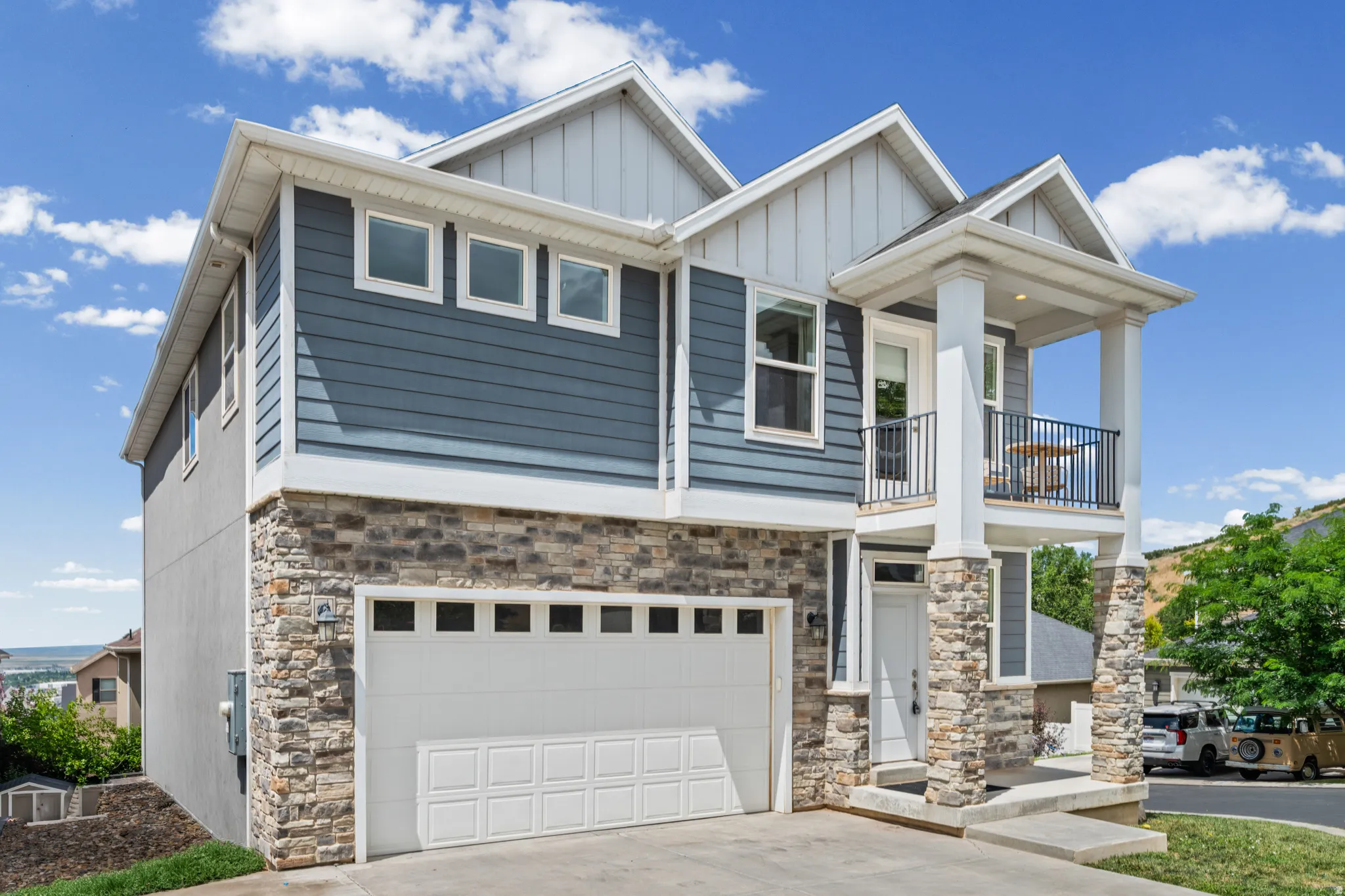 Contemporary exterior featuring mixed-material siding, a two-car garage, and a covered balcony with wrought iron railing