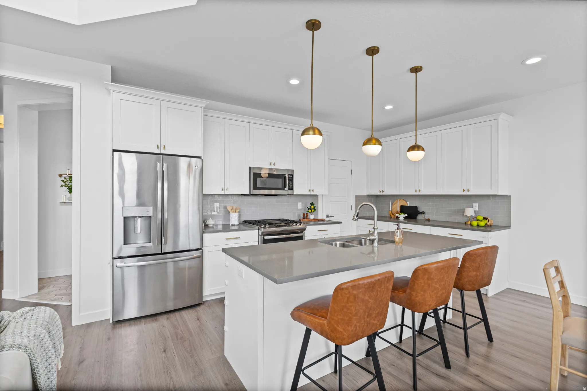 Modern kitchen featuring white cabinetry, stainless steel appliances, a center island with sink, gray countertops, and wood-finish flooring
