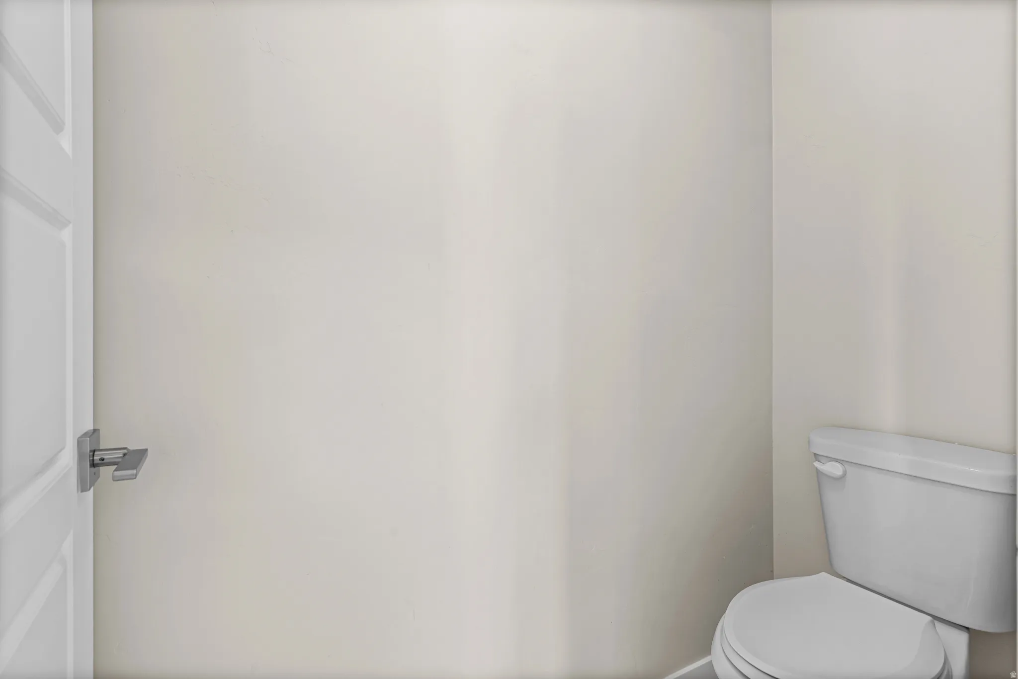Compact water closet featuring a modern white toilet, light-toned walls, and a white paneled door with a contemporary brushed nickel door handle