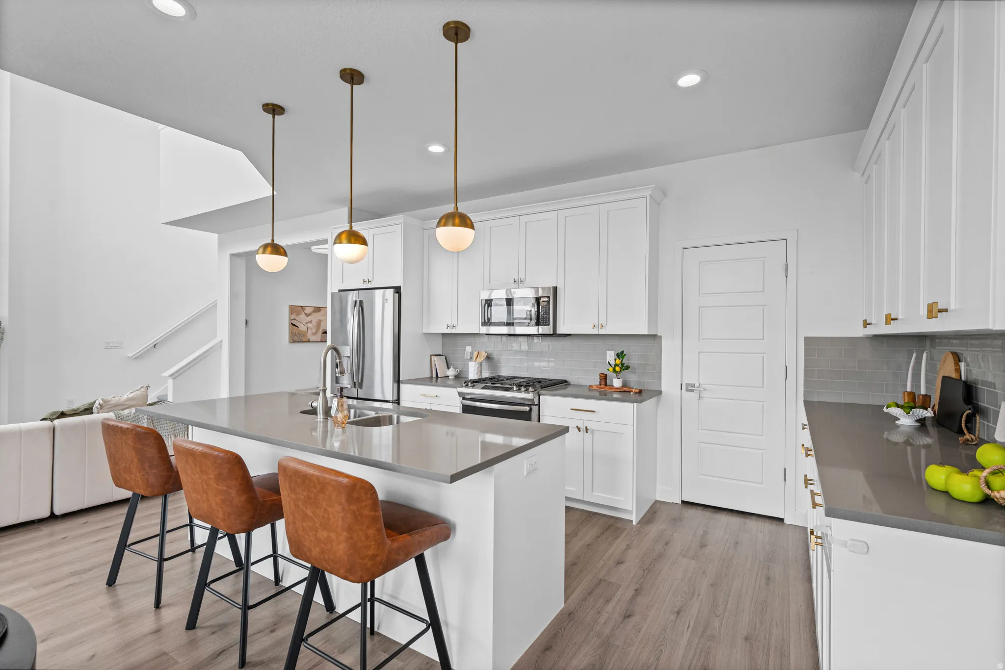 Open-concept kitchen featuring an expansive island with seating, pendant lighting, stainless steel appliances, and wood-finish flooring