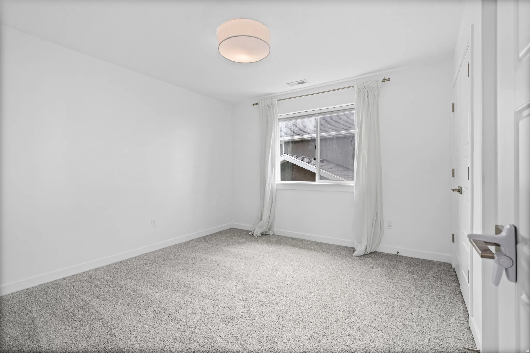 Spacious room featuring neutral carpeting, white walls, a double-hung window, and a contemporary flush-mount ceiling light fixture
