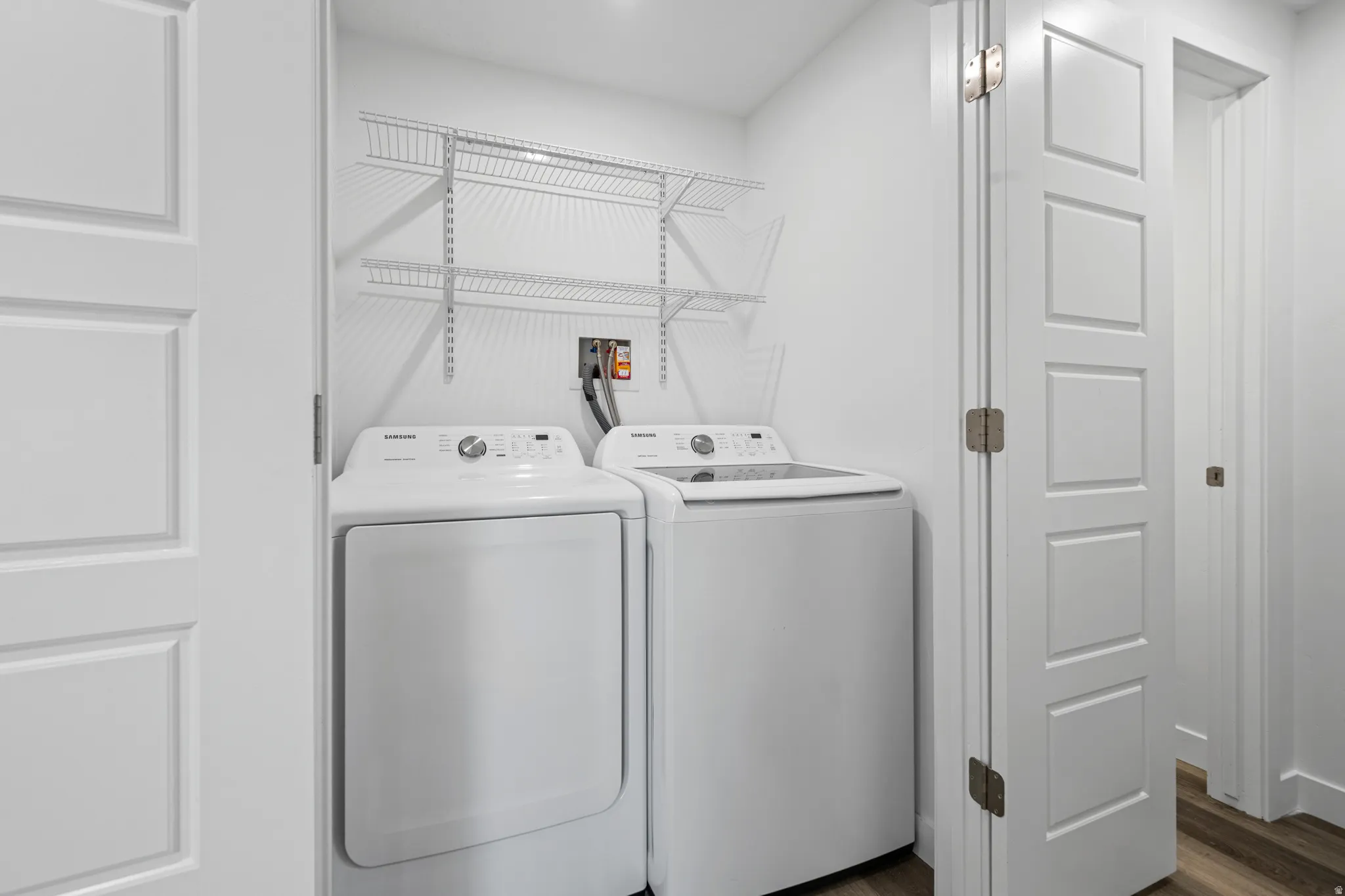 Dedicated laundry area featuring white walls, wood-finish flooring, two large appliances, and wire shelving