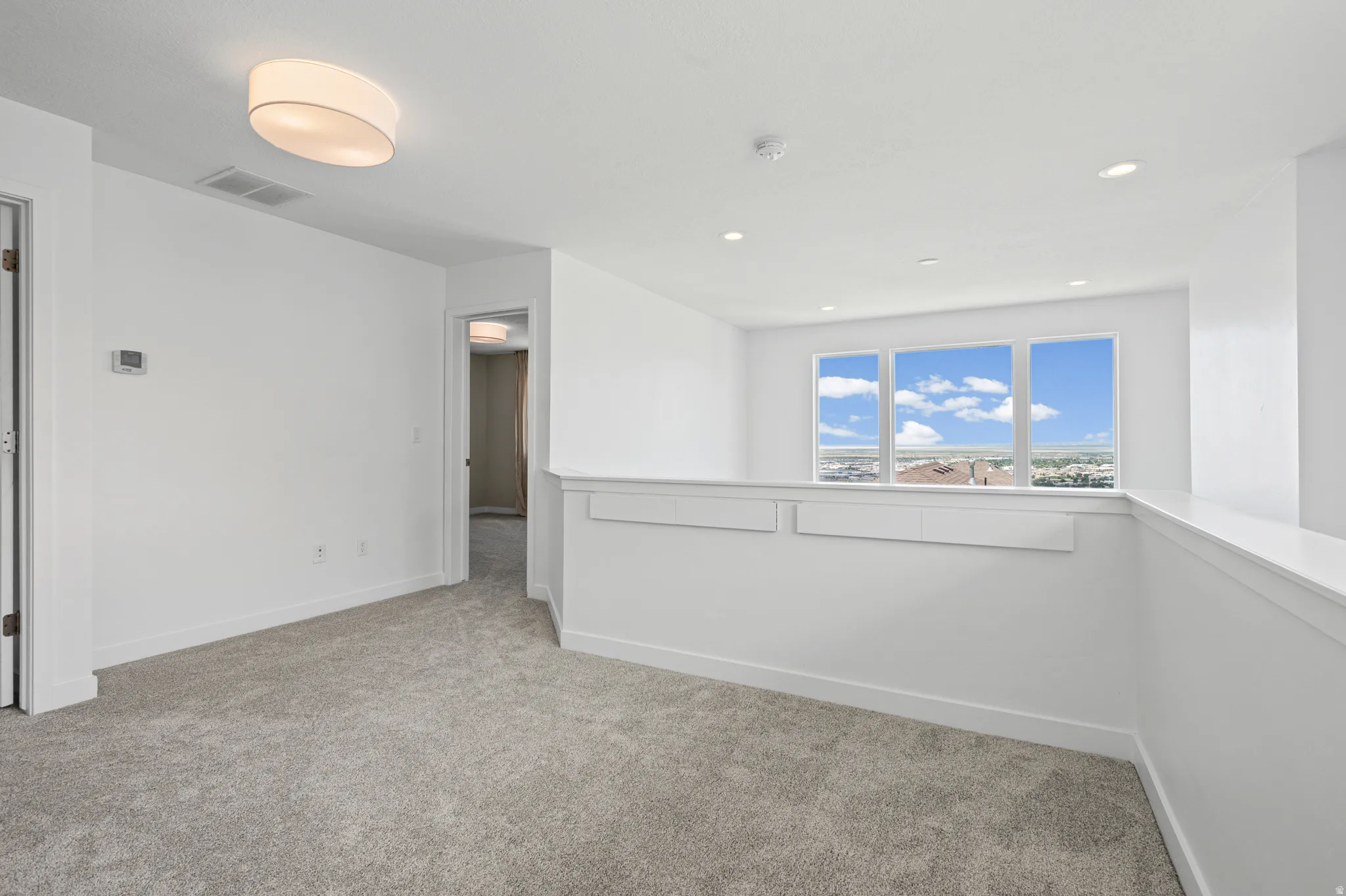 Carpeted upper-level landing featuring a half wall with integrated storage, a trio of large windows with white trim, and recessed ceiling lighting