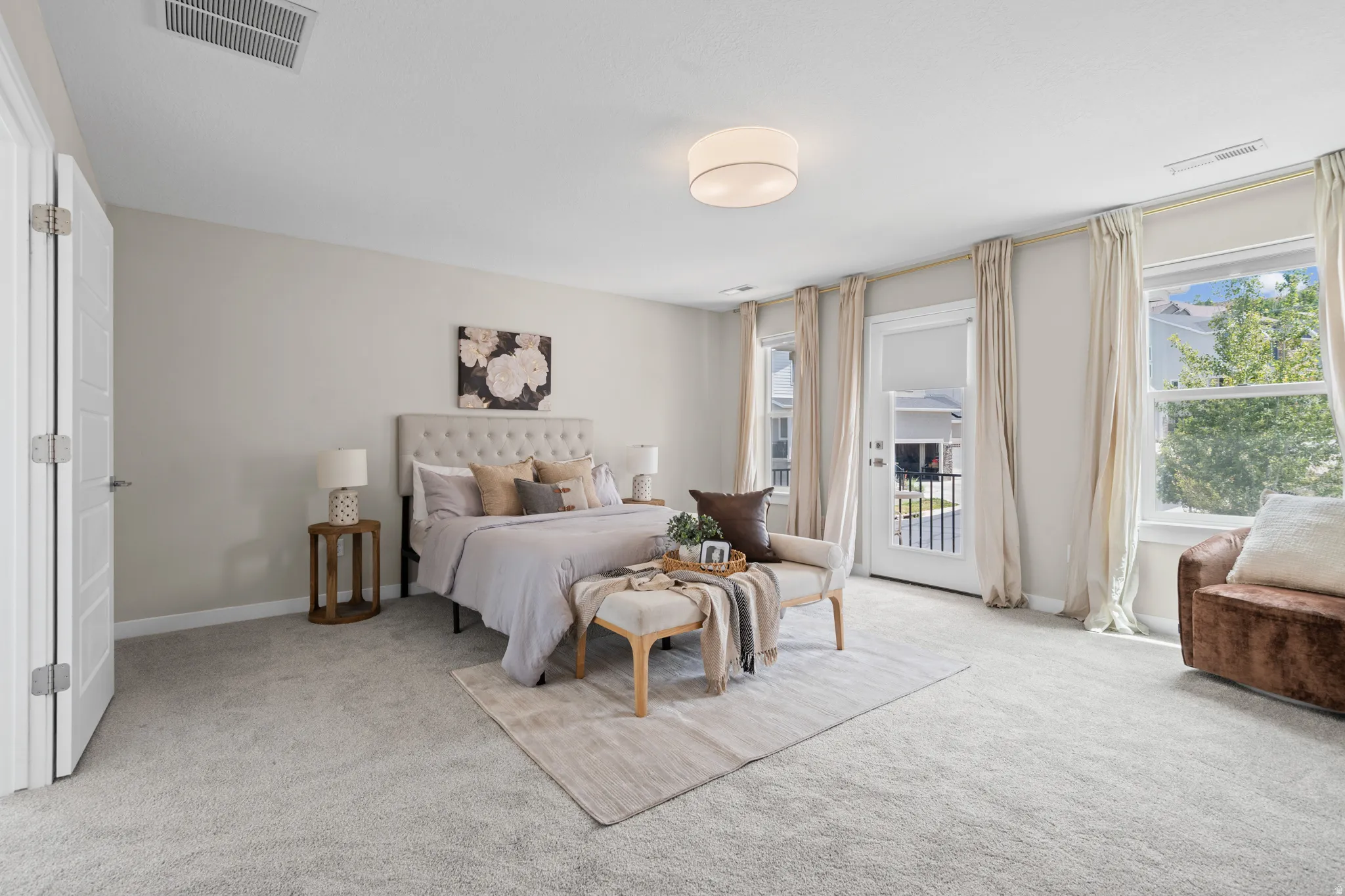 Spacious bedroom featuring light-colored carpet flooring, a ceiling-mounted light fixture, and a large window with a white frame