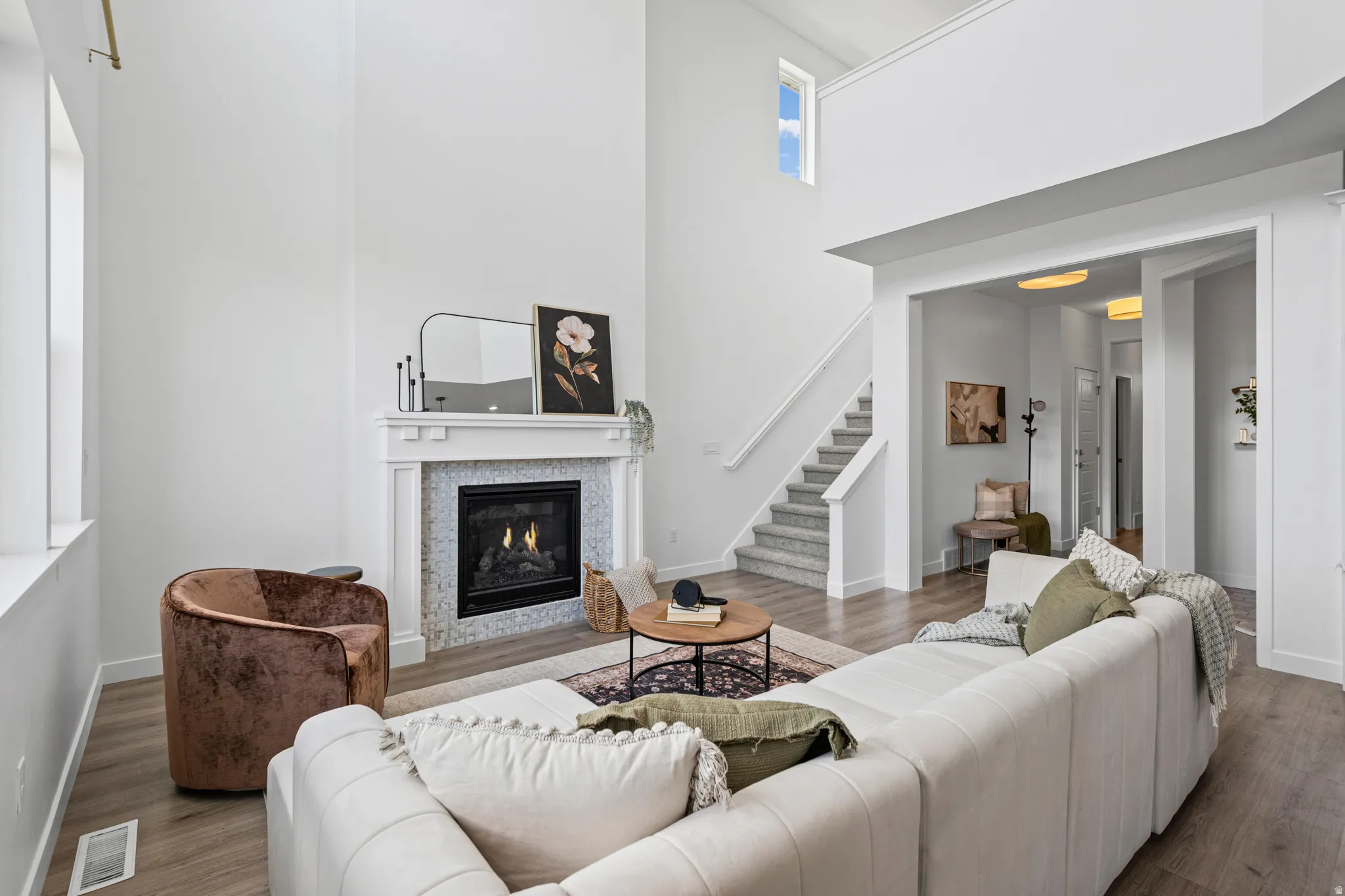 Vaulted ceiling living area featuring a fireplace with a white mantel and mosaic tile surround, wood-finish flooring, and natural light from a large window