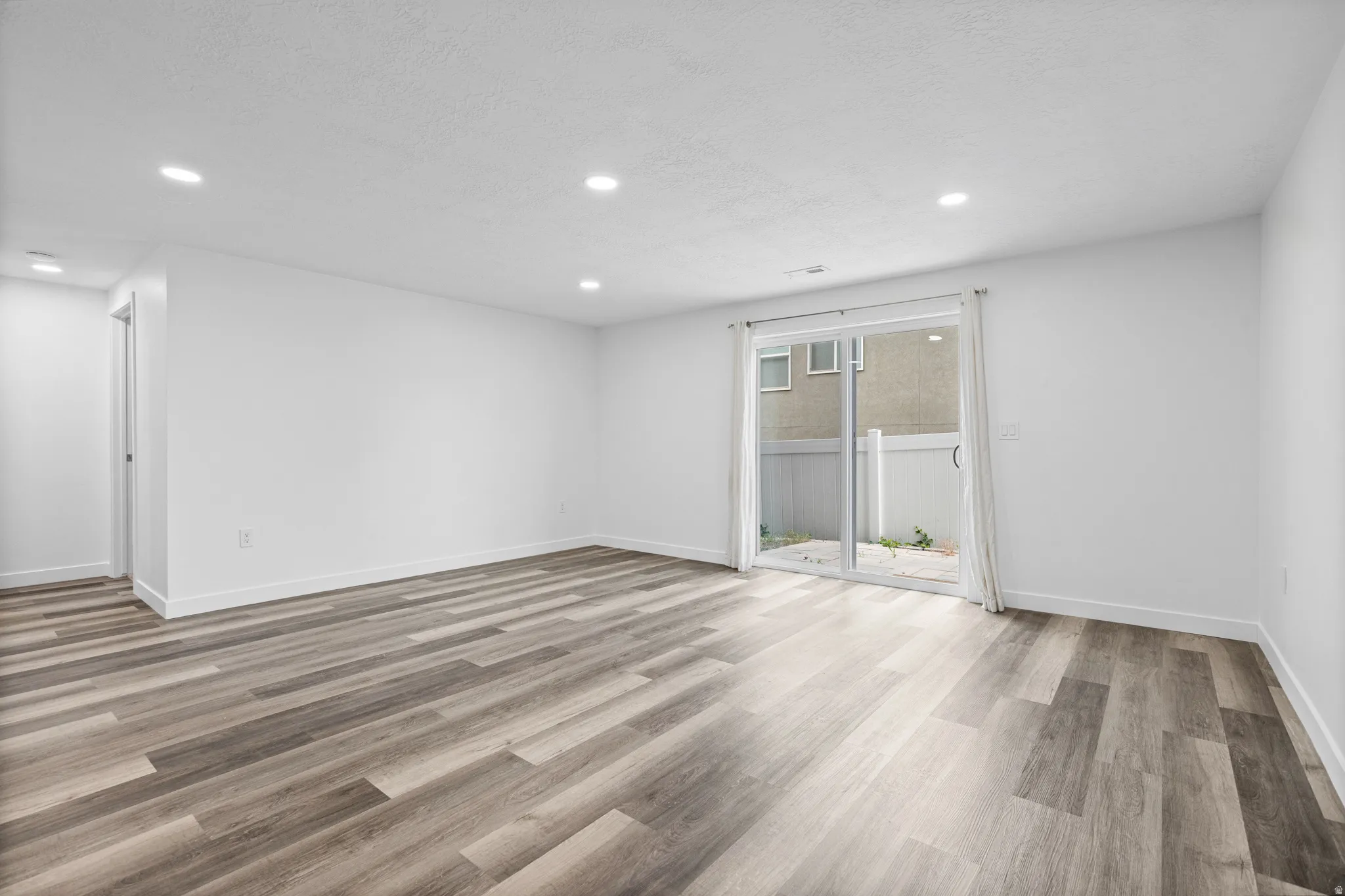 Spacious room featuring wood-finish flooring, recessed lighting, and a sliding glass door providing access to a private outdoor area