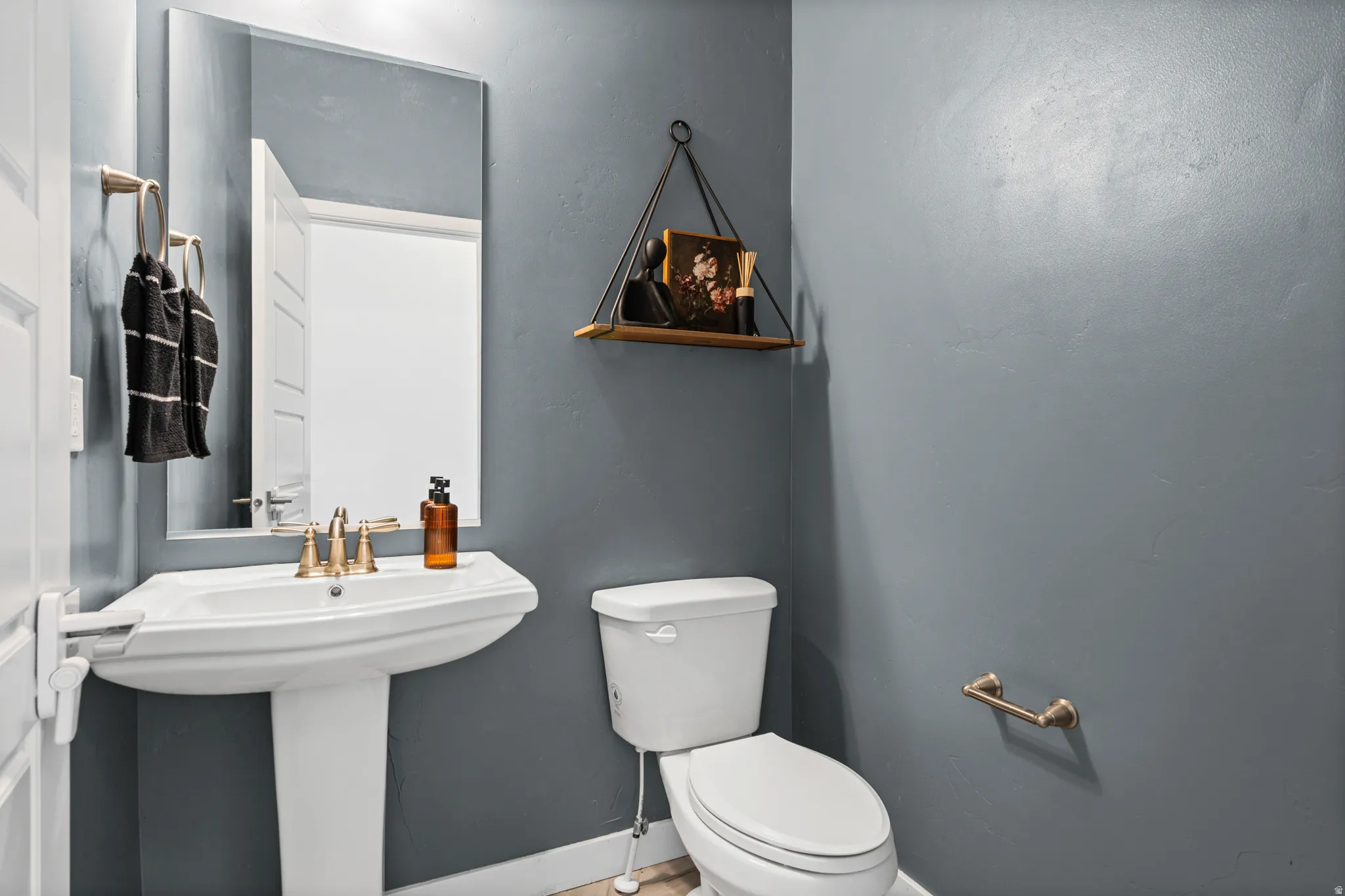 Pedestal sink with brass-finish faucet, toilet, wall-mounted mirror, and brass-finish towel ring