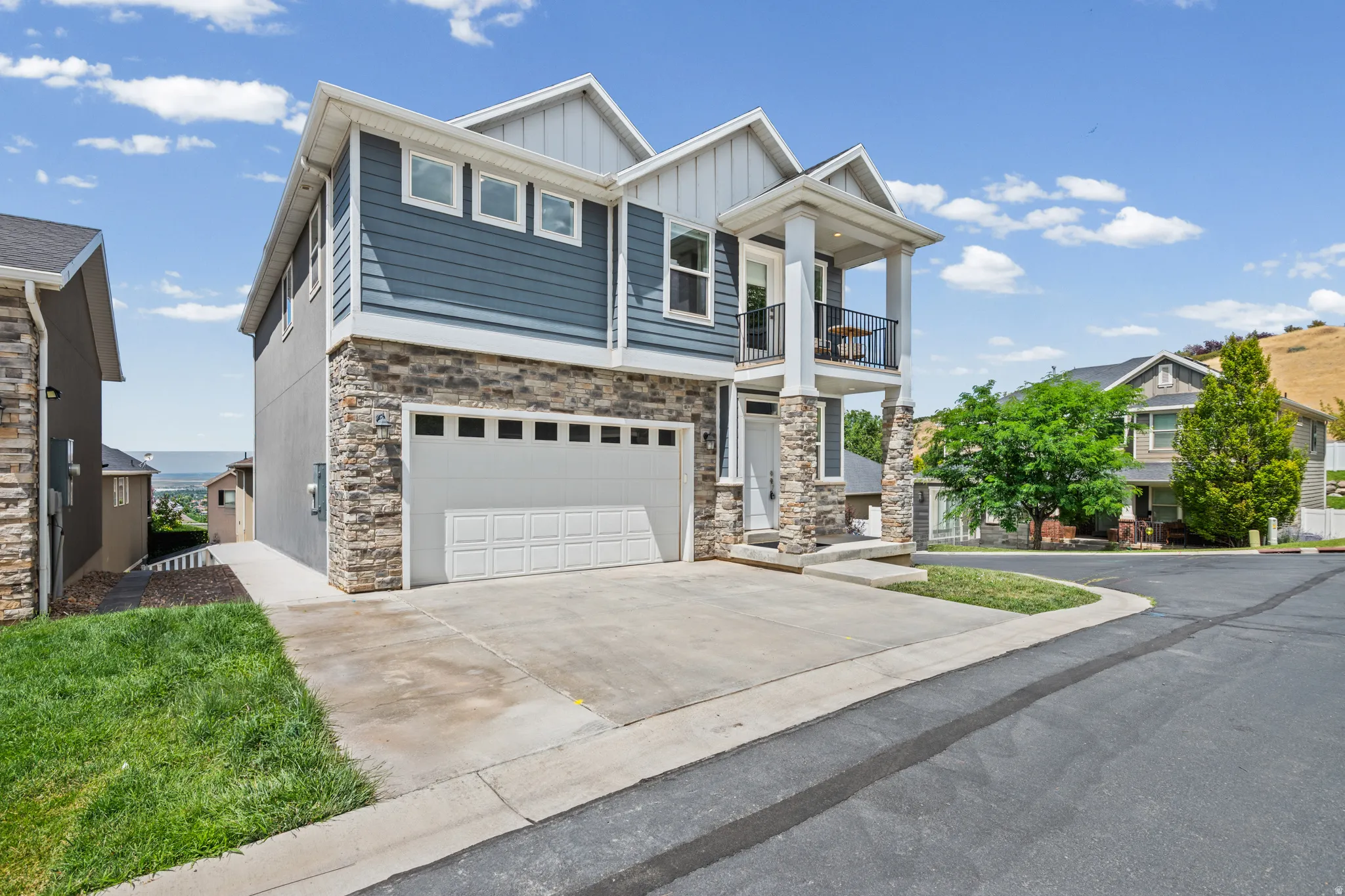 Contemporary residence featuring a two-car garage, stone veneer and horizontal siding façade, covered entry, and an upper-level balcony with metal railing