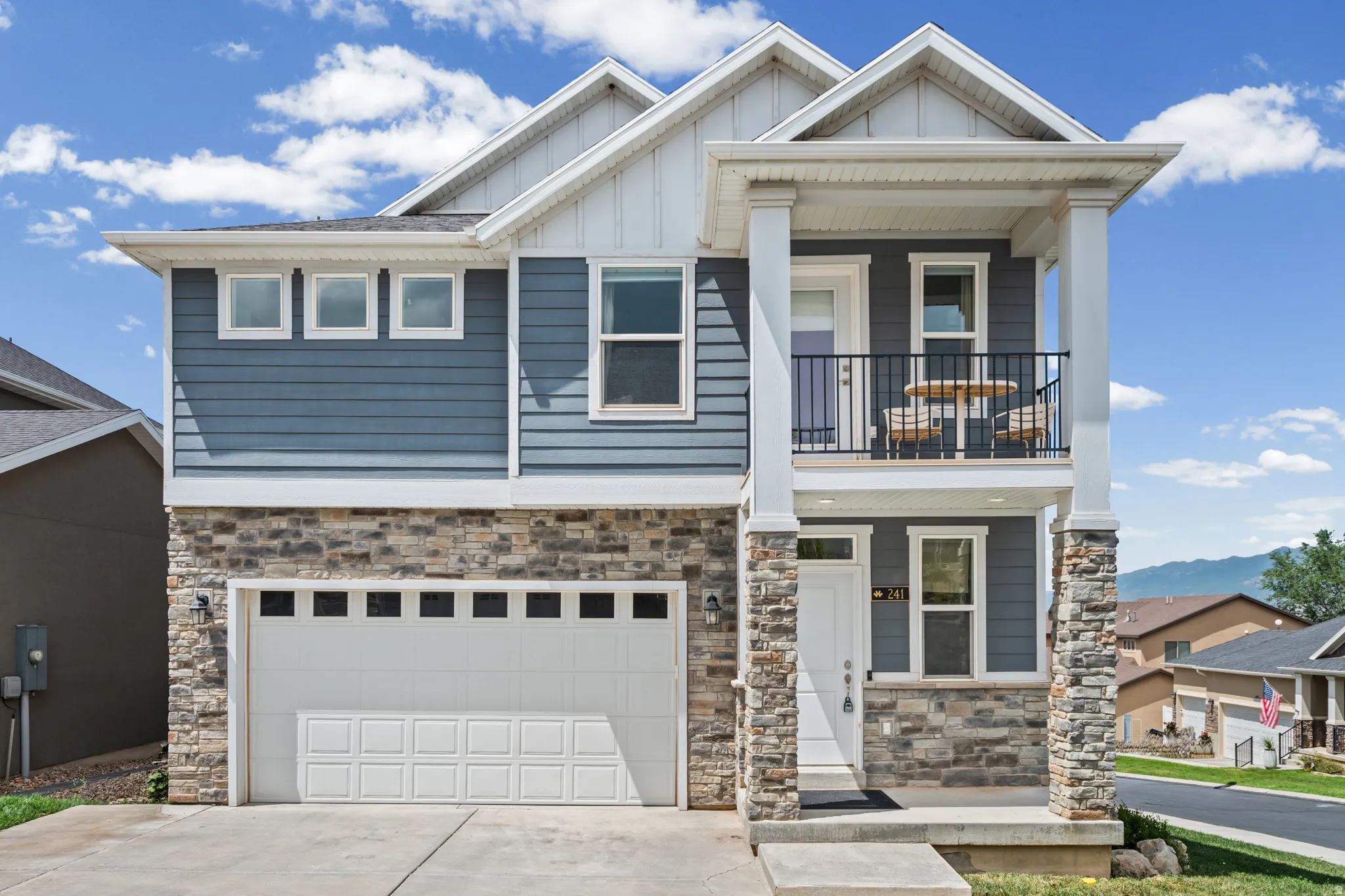 Two-story residence featuring a stone and siding facade, an attached garage, a second-story balcony with metal railing, and a covered entry porch