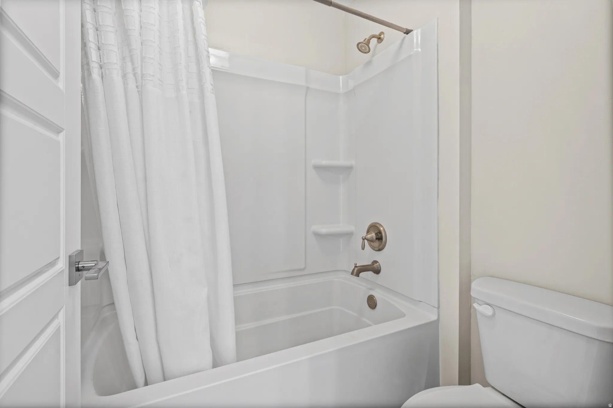 Bathtub and shower combination featuring brushed nickel fixtures and integrated shelving
