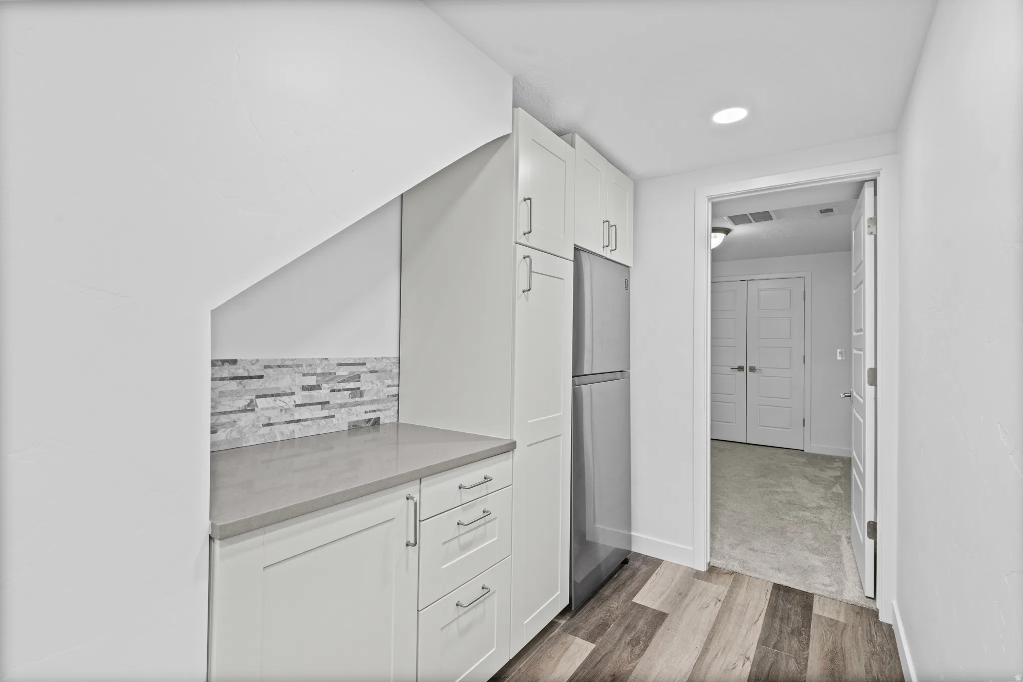 Compact kitchen area featuring white cabinetry, a stainless steel refrigerator, a light gray countertop, and a stacked stone backsplash