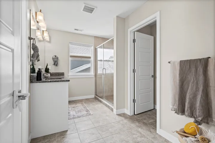 Bathroom featuring a single vanity with stone countertop, tile flooring, glass-enclosed shower, and a large window providing natural light