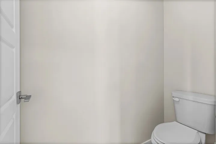 Compact water closet featuring a modern white toilet, light-toned walls, and a white paneled door with a contemporary brushed nickel door handle