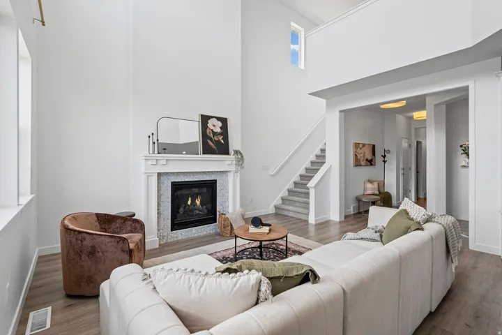 Vaulted ceiling living area featuring a fireplace with a white mantel and mosaic tile surround, wood-finish flooring, and natural light from a large window