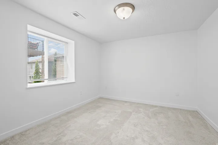 Bright room featuring light grey carpeting, white walls, and a single window with blinds