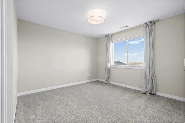 Neutral-toned room featuring a large window with distant scenery, light gray wall-to-wall carpeting, white baseboards, and a contemporary ceiling light fixture