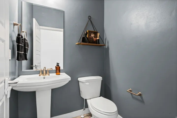 Pedestal sink with brass-finish faucet, toilet, wall-mounted mirror, and brass-finish towel ring
