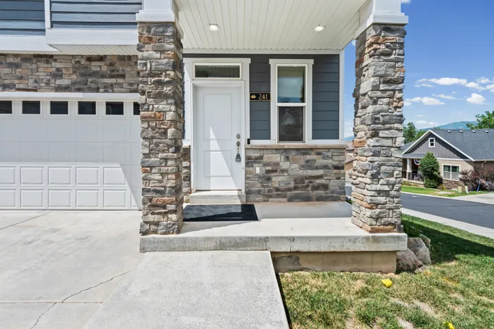 Exterior featuring a white front door with transom window, stone veneer accents, dark siding, white garage door with upper window panels, and a concrete driveway