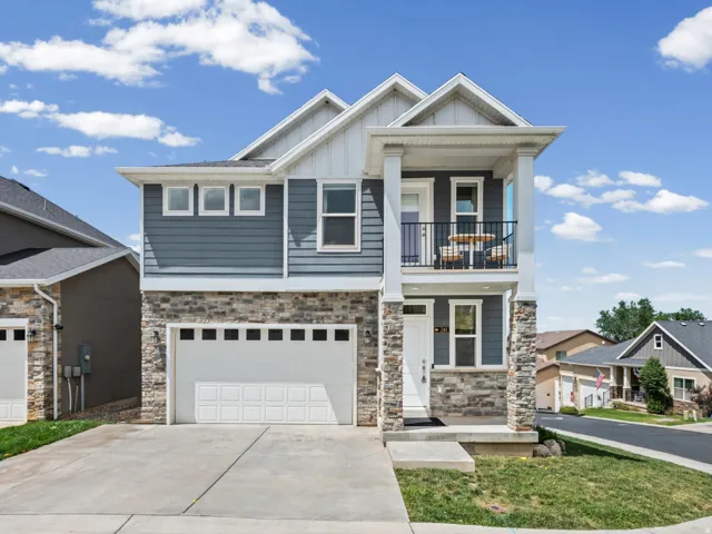 Contemporary two-story exterior featuring blue siding, stone veneer accents, an attached two-car garage, and a second-story balcony