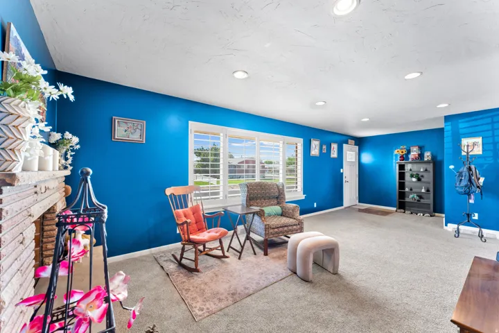 Spacious room featuring blue walls, recessed lighting, carpet flooring, a large window with white louvered shutters, and a brick fireplace