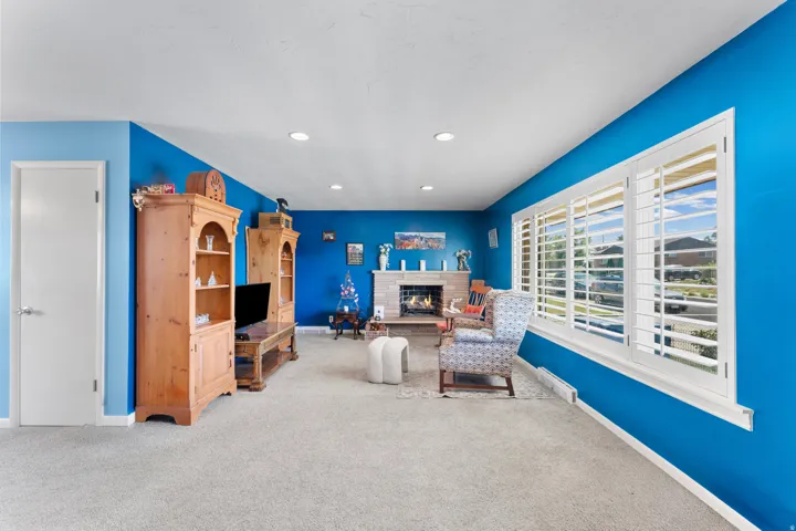 Living area featuring plush carpeting, a stone-surround fireplace with a wood mantle, and recessed ceiling lighting
