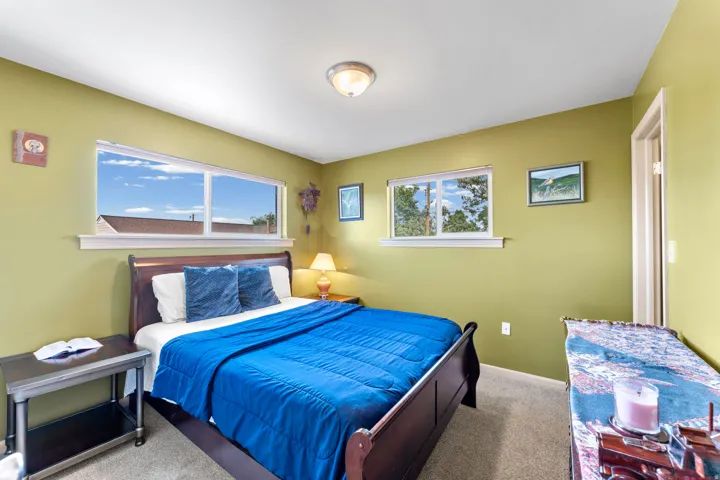 Recessed lighting illuminates a bedroom featuring two windows, neutral carpet flooring, and a door frame