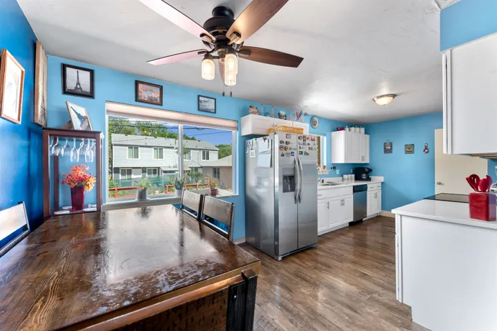 Open-concept kitchen and dining area featuring wood-finish flooring, white cabinetry, stainless steel appliances, and a ceiling fan with integrated lighting