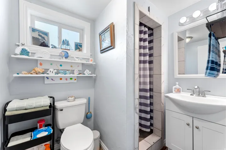 Bathroom featuring a window with natural light, integrated wall shelving, a white toilet, a shower stall with tiled walls, and a vanity with a basin sink and a mirror