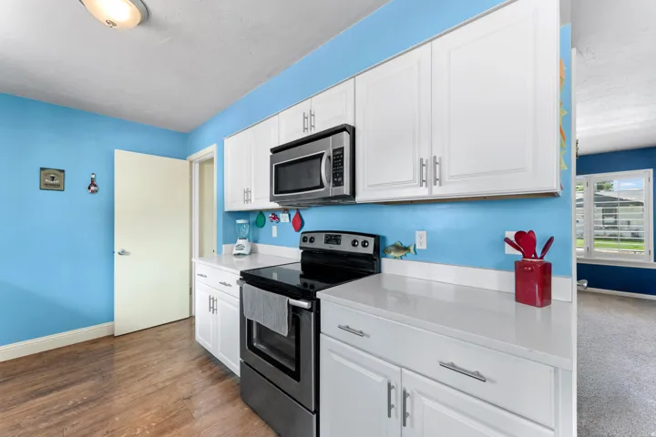 Kitchen featuring white cabinetry, stainless steel microwave, black range, white countertops, and wood-finish flooring