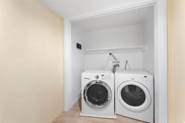 Dedicated laundry area with a white shelving unit, light-toned walls, and wood-finish flooring