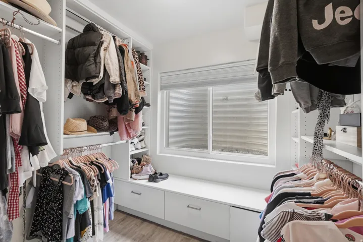 Custom closet system featuring built-in shelving, multiple hanging rods, integrated drawers, and a window with a privacy blind