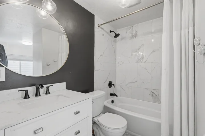 Bathroom featuring a white vanity with an integrated sink, matte black faucet, and a round wall-mounted mirror with decorative lighting