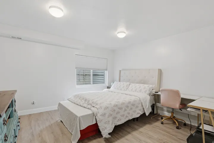 Bright room featuring wood-finish flooring, a window with a roller shade, and overhead flush-mount lighting fixtures